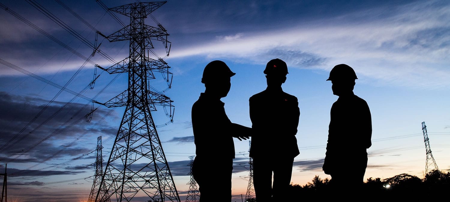 Ingenieros en obra junto a torres de alta tensión al atardecer